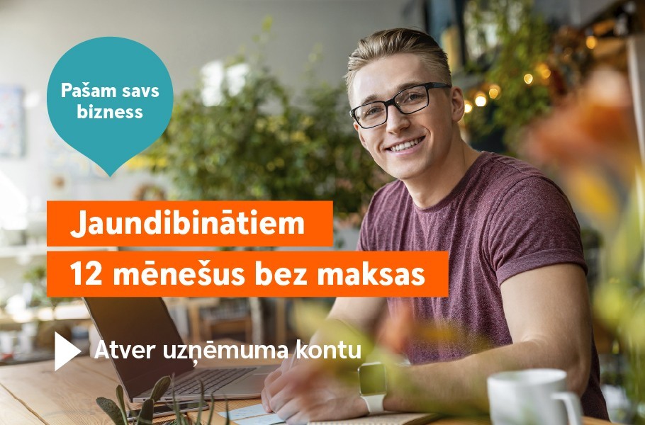 Jauns vīrietis smaidīgs skatās kamerā, sēžot pie datora